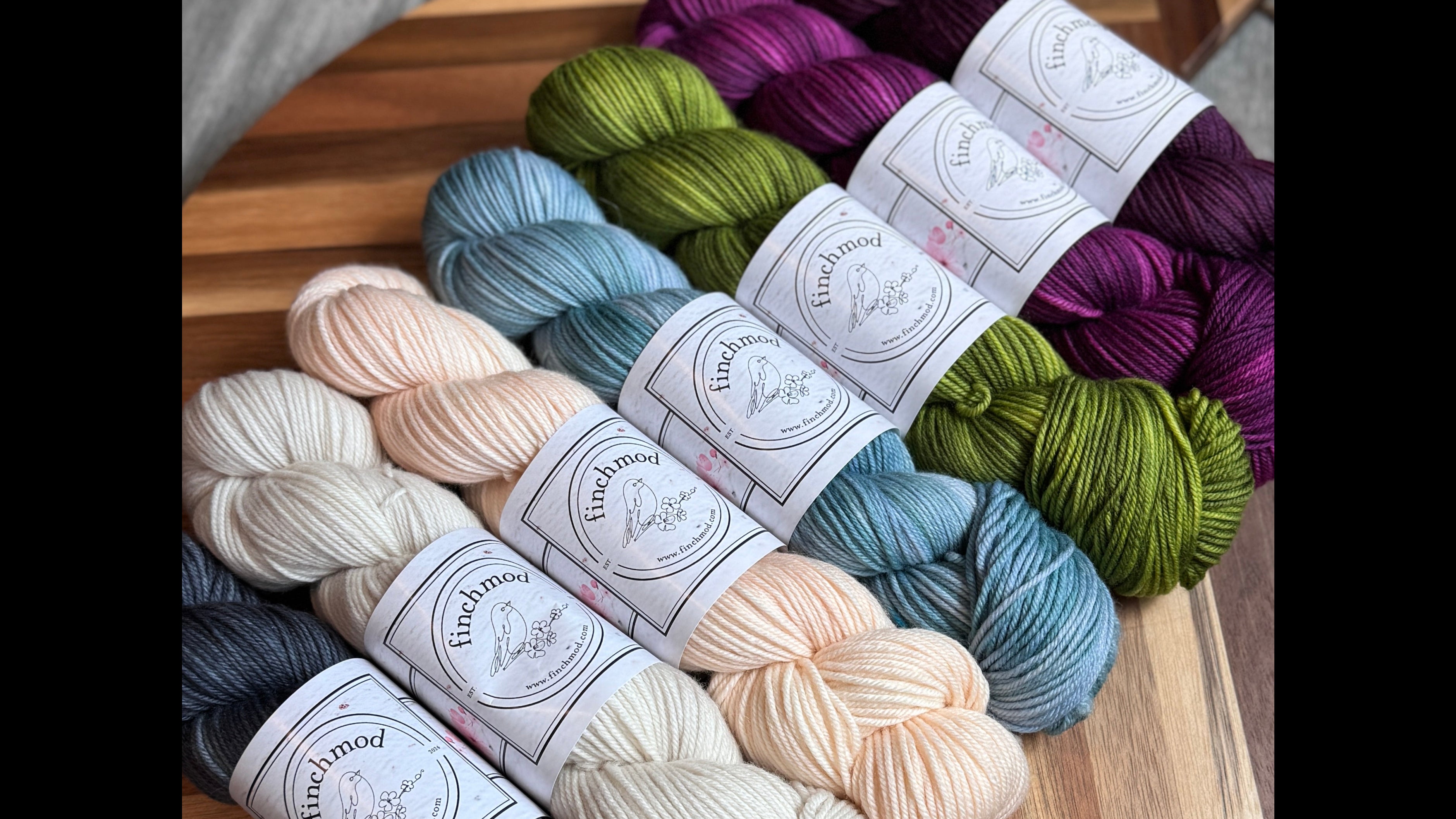 Assorted skeins of yarn on a wooden board with a gray floor background
