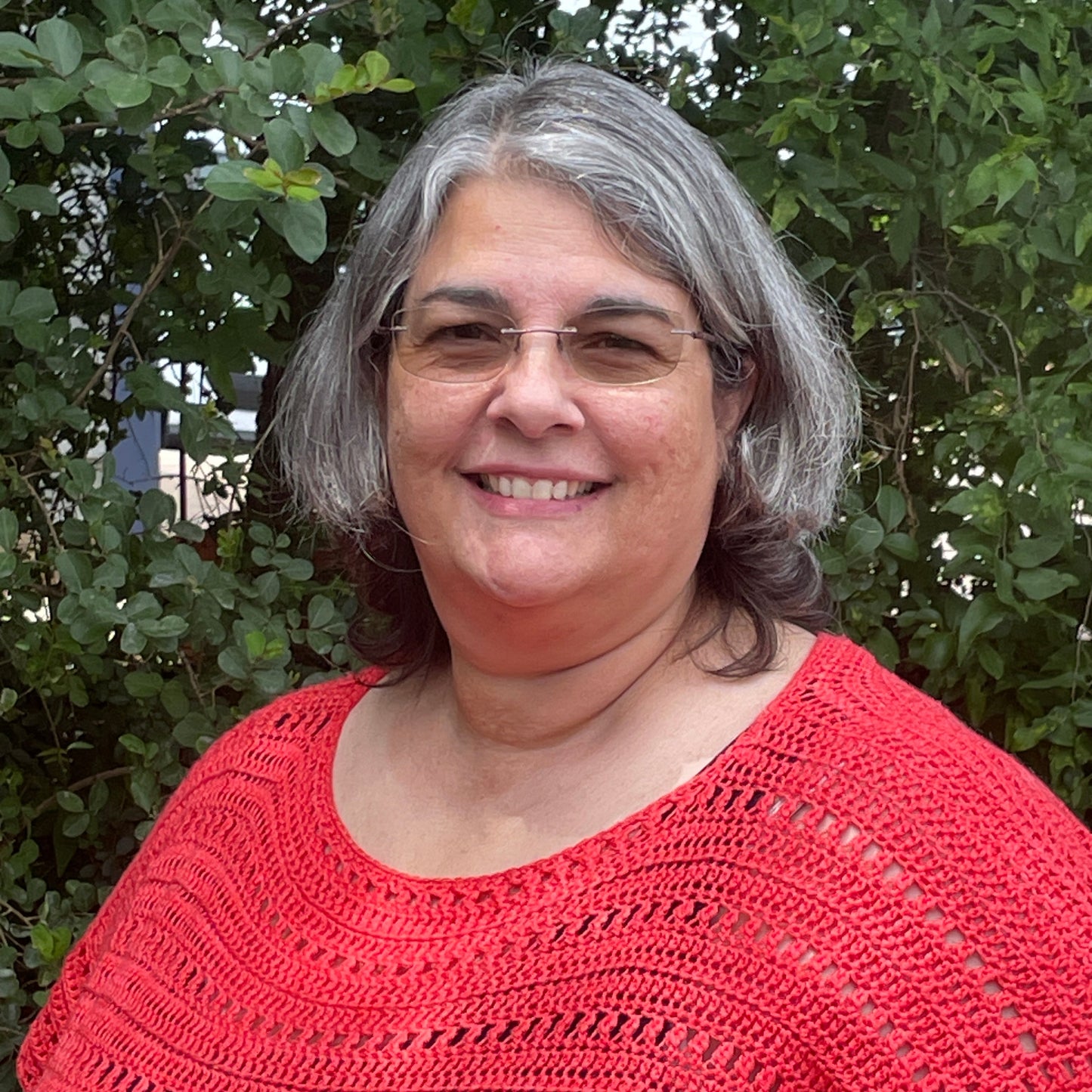 Woman wearing a red knitted sweater standing in front of green foliage
